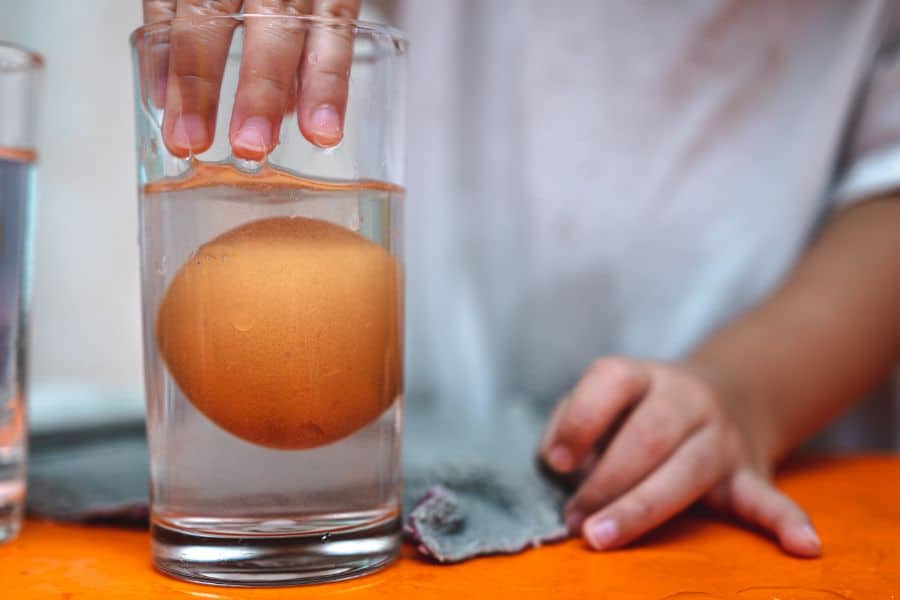 A glass of water with an egg in it conducting the float test. 