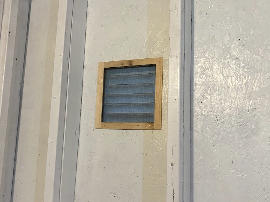 The window screen in place over the vent secured with a wooden frame. 