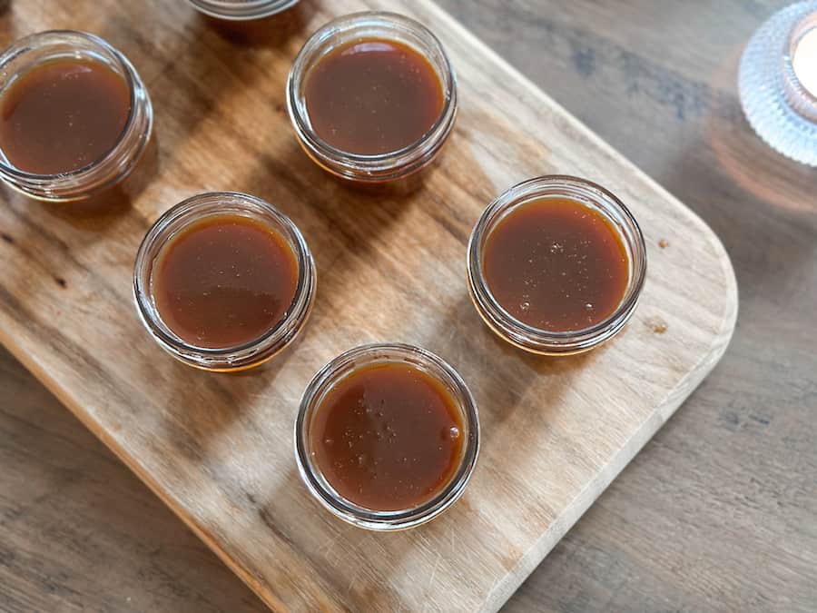 Five small mason jars filled with homemade caramel without the lids on. 