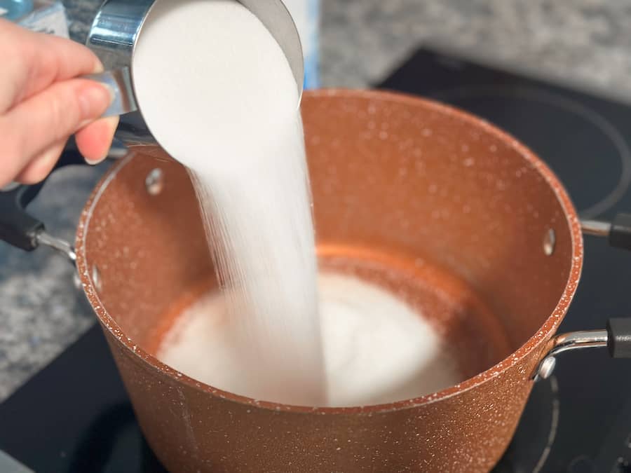 Pouring granulated sugar into a copper coloured pot to make homemade salted caramel.