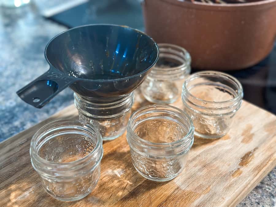 Empty small mason jars with a funnel ready to be filled with homemade salted caramel.