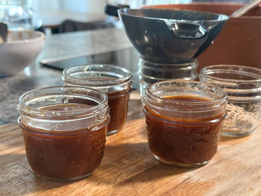 Small glass mason jars being filled with homemade salted caramel using a funnel.