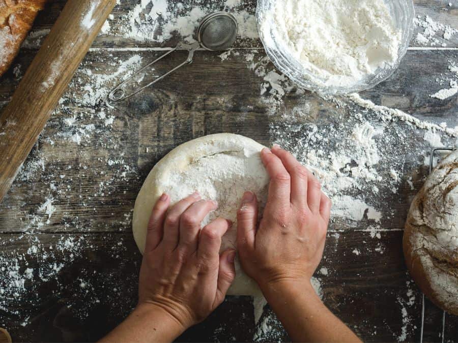Womens hand folding bread dough on a counter with flour on it.
