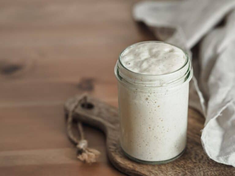 A glass jar of sourdough starter on a wooden board.