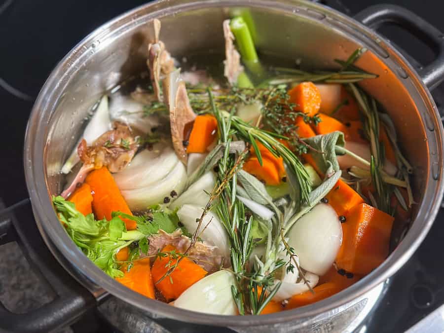 Vegetables, herbs and a turkey carcass in a large stock pot to make turkey bone broth. 