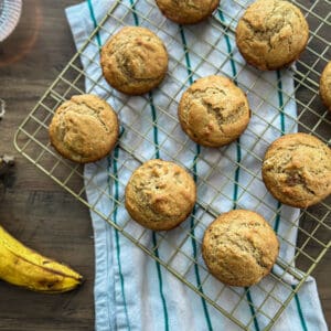 Gluten-Free Banana Bread Muffins on a gold cooling rack with a striped tea towel and two bananas beside it