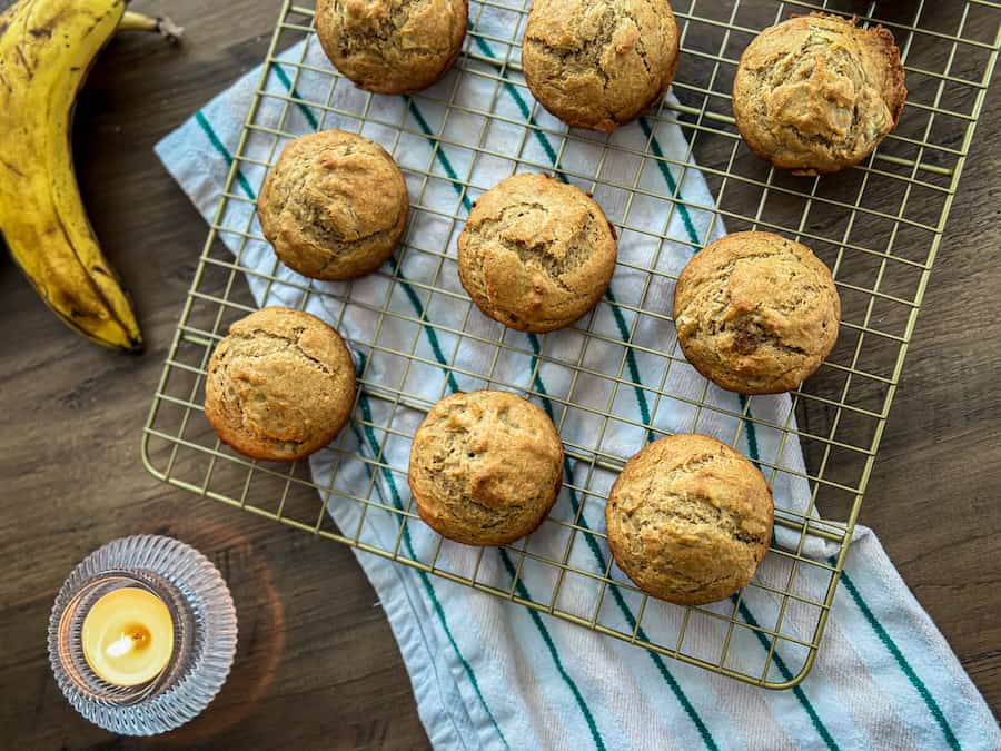 Gluten-Free Banana Bread Muffins on a gold wired cooling rack with a stripped tea towel underneath and a small candle lit nearby. 