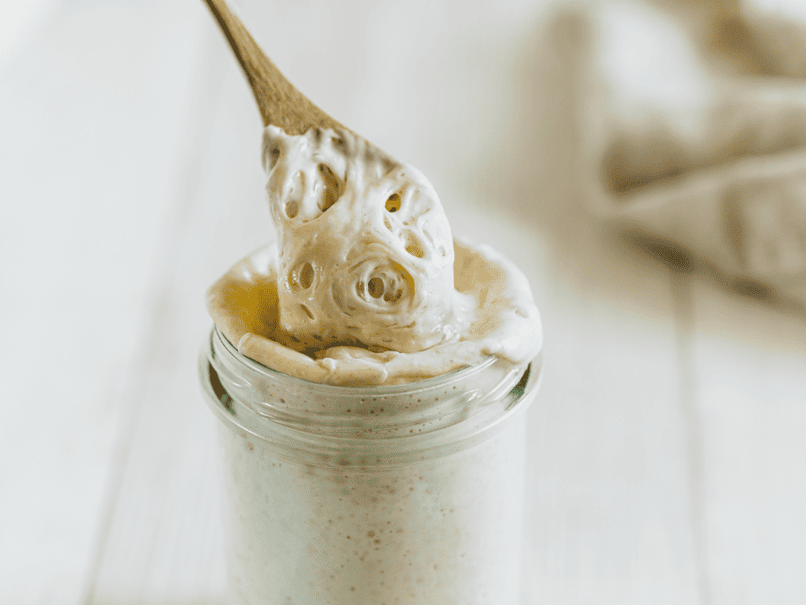 Ready to use sourdough starter in a glass jar with a wooden spoon scooping some out. 