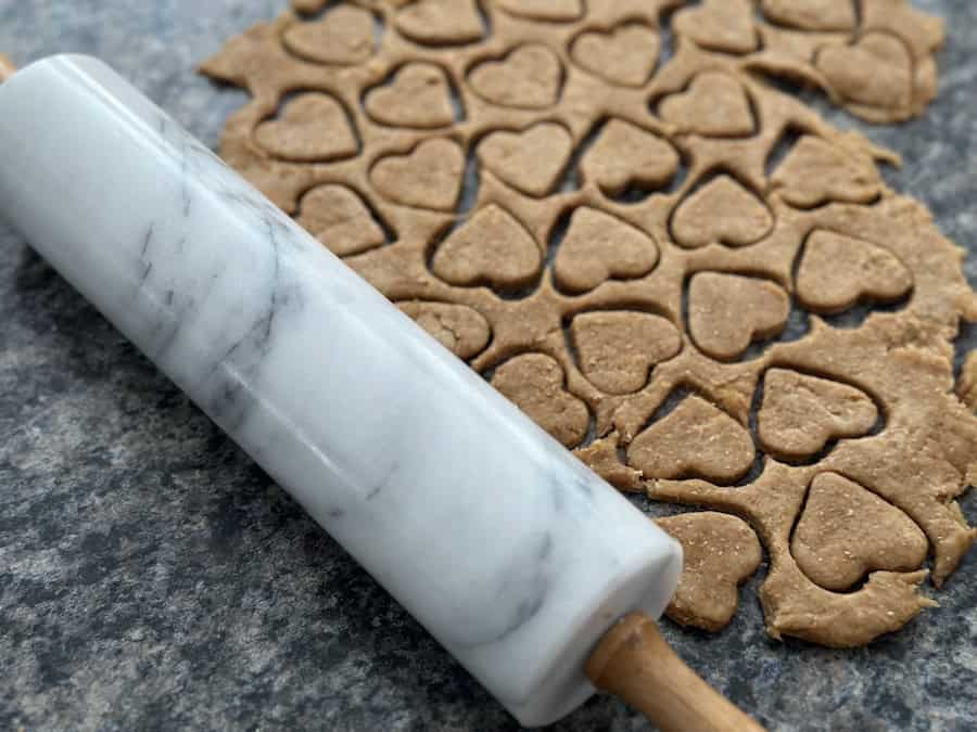 A marble rolling pin beside rolled homemade dog treat dough with hearts cut out using a cookie cutter.